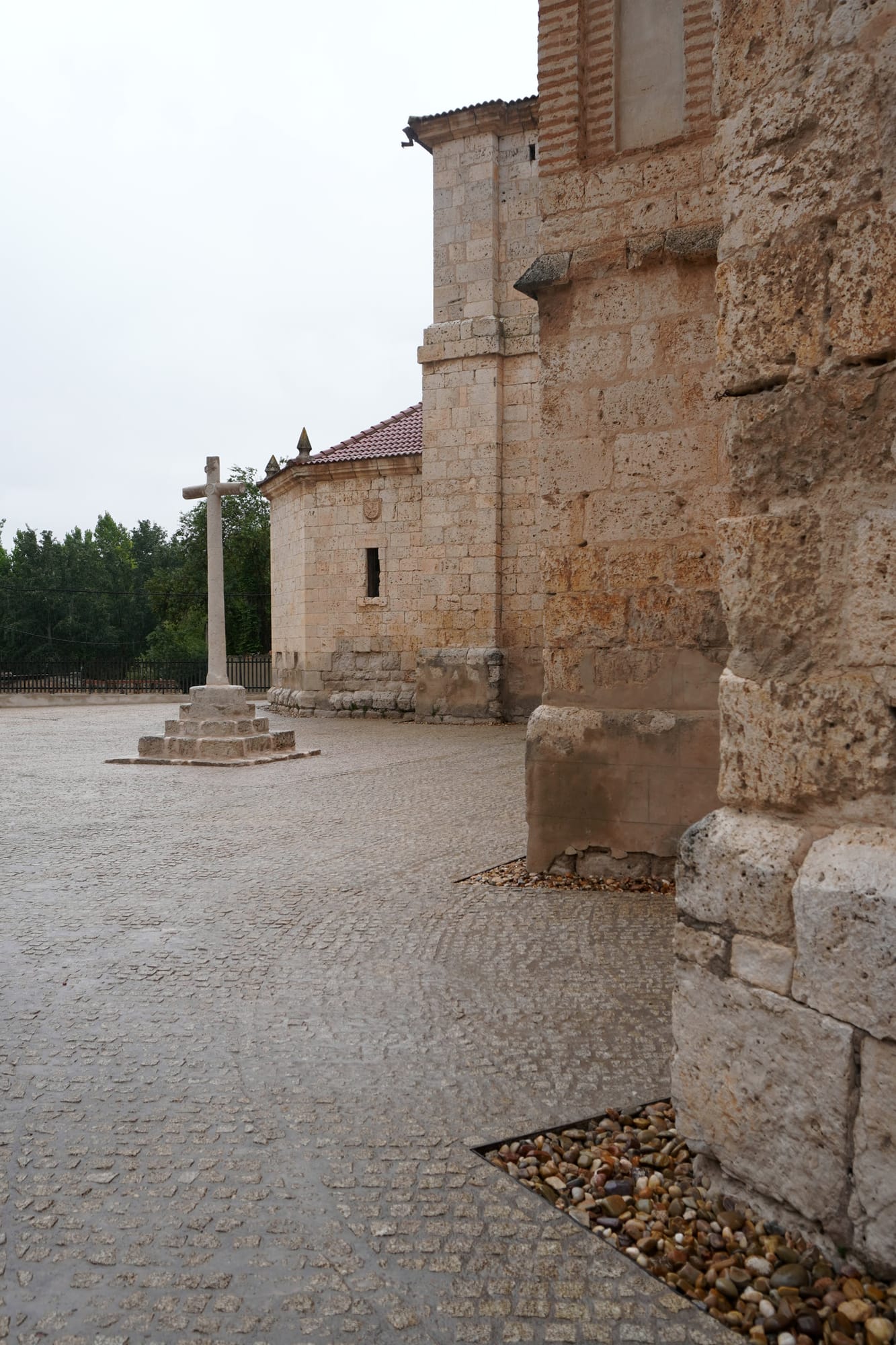 Adoquinado junto a los contrafuertes de piedra de la iglesia, con el crucero al fondo