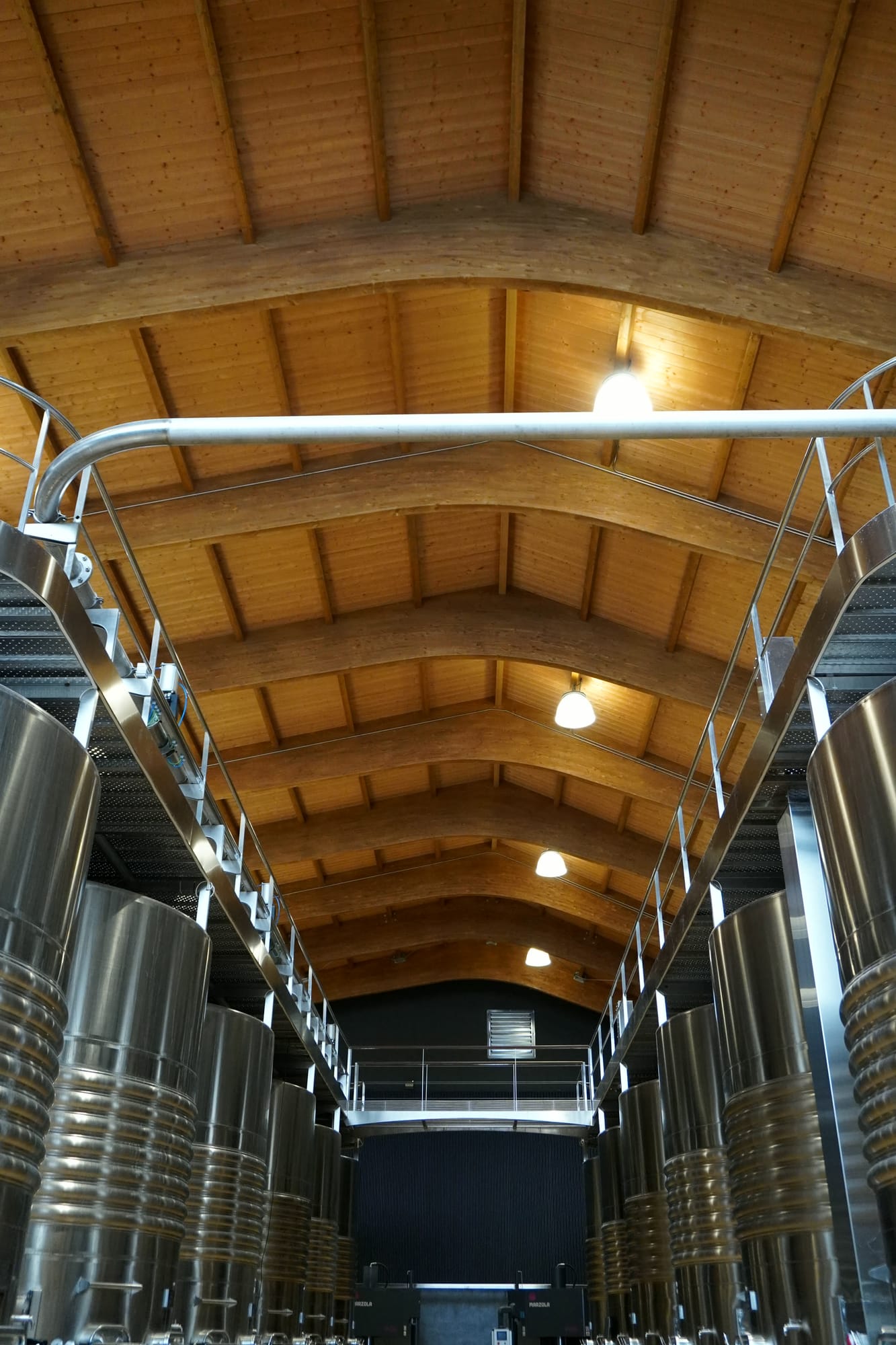 Nave de bodega con dos filas de depósitos de acero inoxidable bajo una bóveda de vigas de madera